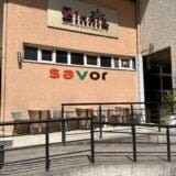 Exterior view of Savor restaurant with outdoor seating and a beige wall with the "savor" sign.