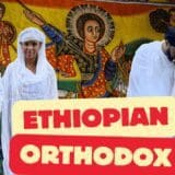 People in traditional white Ethiopian Orthodox clothes by a religious mural.