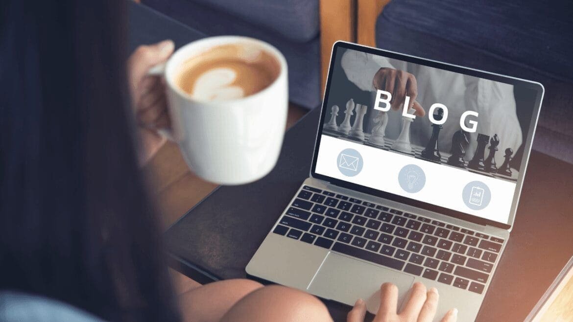 Person holding coffee while viewing blog on laptop.