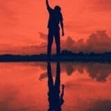 A person with arms rasised, reflected on calm water, symbolizing self-growth, personal freedom and mental health healing.