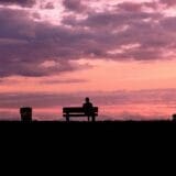 Adult sitting alone on a park bench at sunset, reflecting on loneliness in adulthood
