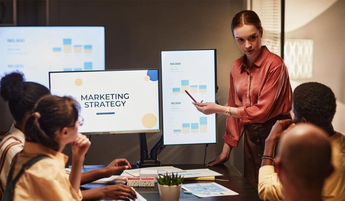 Group of people gathered around a table analyzing marketing statistics on paper and digital devices