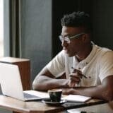 Man working on a laptop in a café with a notebook and coffee.