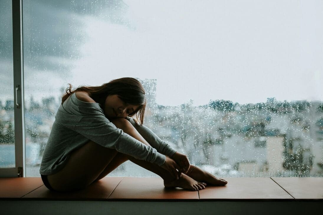 Person embracing herself near a window, embracing forgiveness and managing grief after a Bipolar II diagnosis