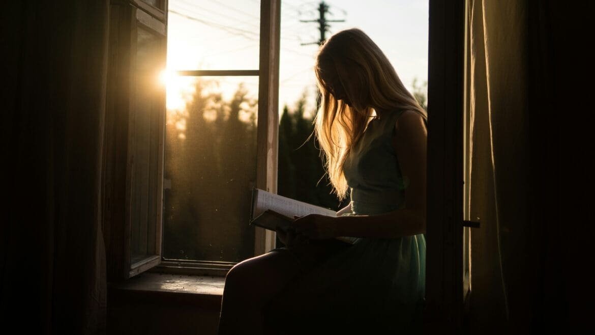 Person journaling by a sunlit window, reflecting on mindset and personal goals with quiet focus
