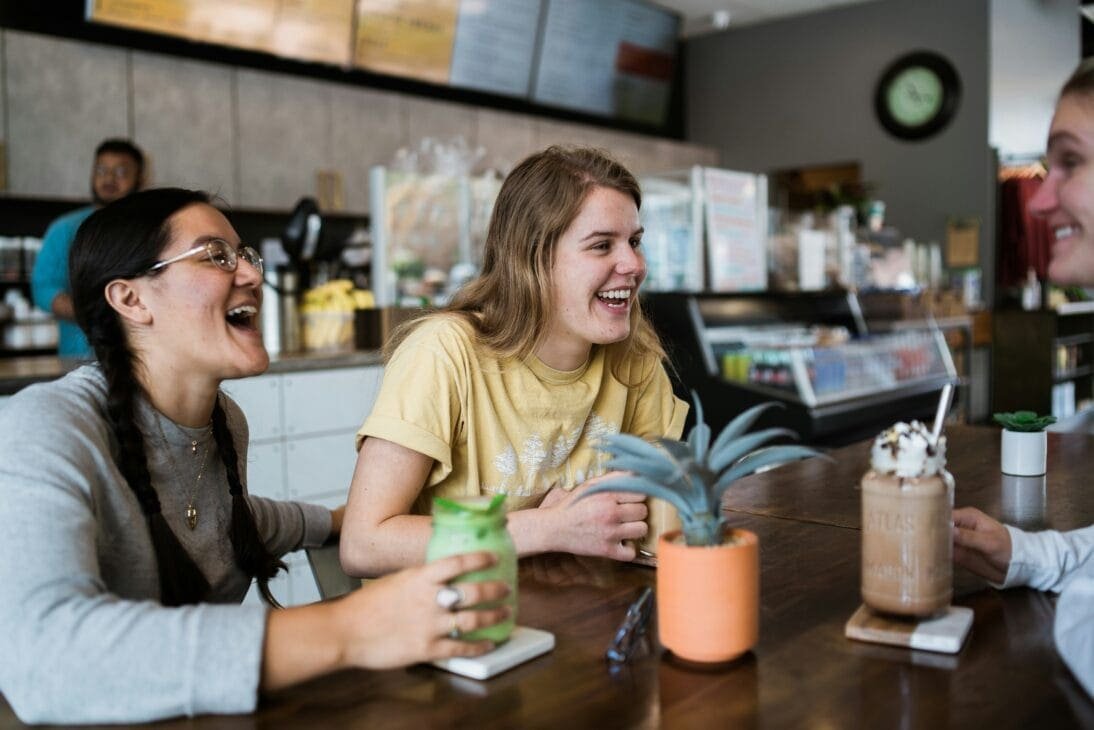 Three adult friends reconnecting over coffee after months apart
