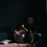 Woman near the window with hands on her face, showing mental health red flags and early signs of burnout