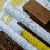Three rolled nautical maps with coastal and oceanic details placed on a wooden table beside a small wooden box.