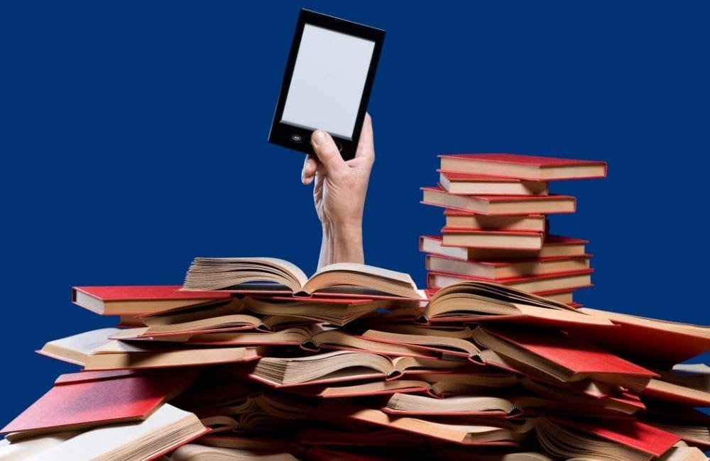 An image of a person holding up an eReader from a stack of books.