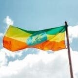 The national flag of Ethiopia with green, yellow, and red stripes and a blue emblem in the center, waving against a blue sky with clouds.
