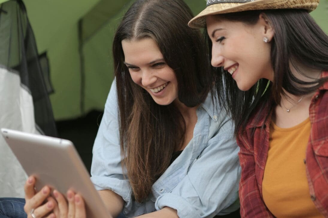Two young women laughing while looking at a computer screen, representing enjoyment and engagement with humorous content