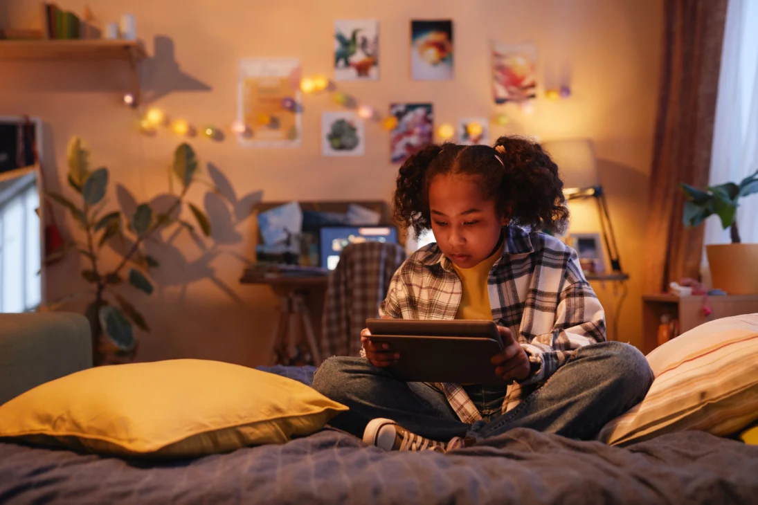 Young Gen Alpha girl sitting in bed using a tablet, reflecting the rise of Gen Alpha trends in digital coping and screen time habits