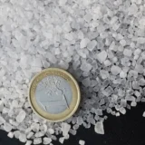 Close-up of coarse salt crystals next to a Euro coin for size comparison.