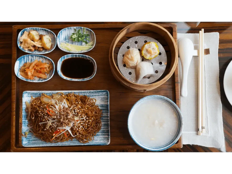 Chinese breakfast featuring congee, steamed buns, and a variety of dim sum dishes.