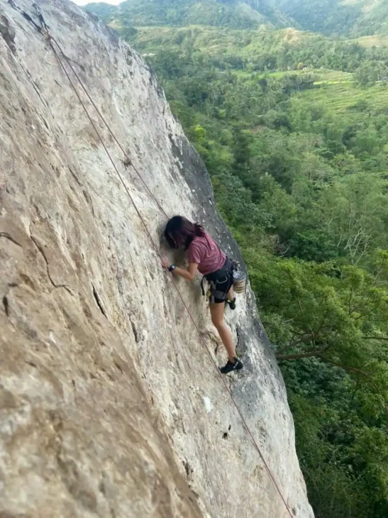 Leigh rock climbing on a steep cliff, showing how investing in experiences builds courage and lasting memories.