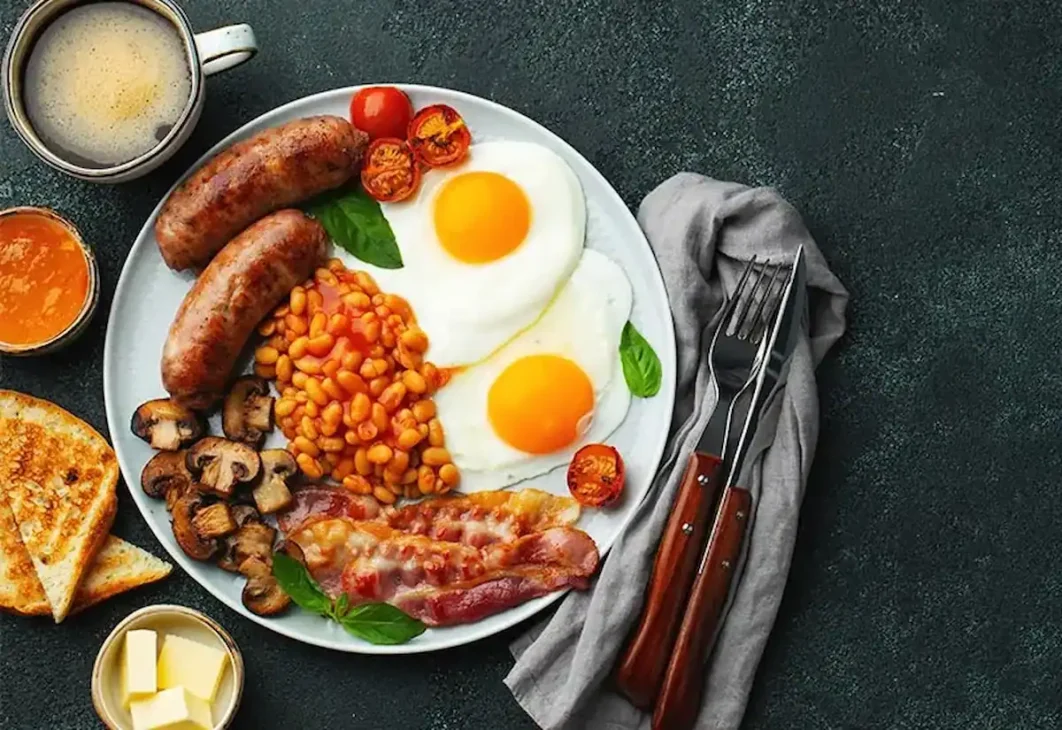 Full English breakfast with eggs, bacon, sausages, baked beans, mushrooms, and toast.