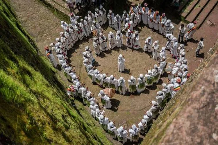 A group of young girls wearing matching white outfits form a large circle, singing together in a gospel-style choir, right outside the Ethiopian Orthodox church, during Ashenda festival season.