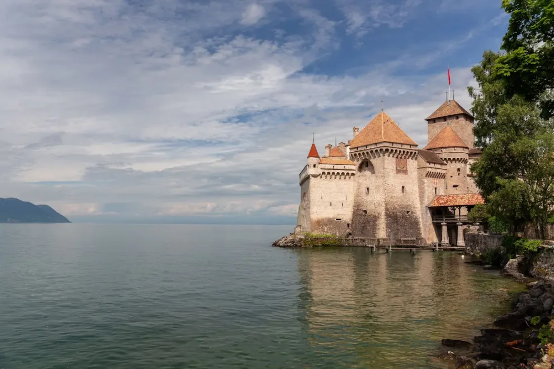Panoramic view of Lake Geneva with sailboats, surrounding mountains, and the city skyline on a sunny day.