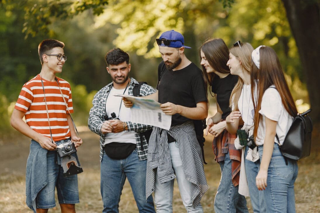 A group of smiling friends on a forest hike, with one man holding a map as they plan their adventure.