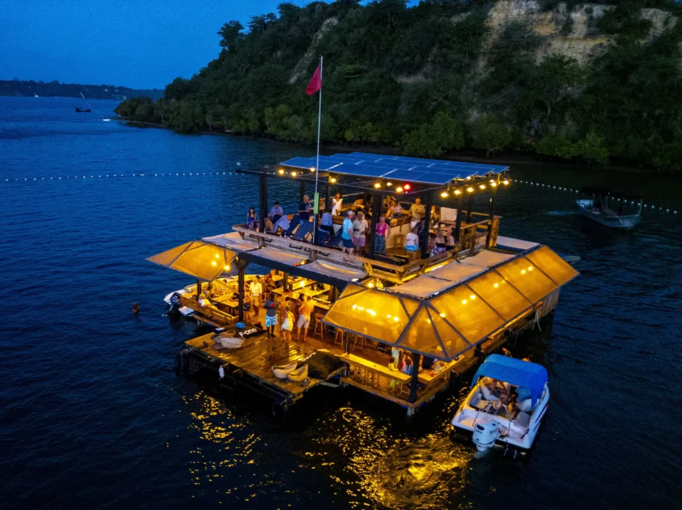 The Muringa Floating Restaurant in Kilifi at night, showing people socializing on the two-level wooden raft illuminated by warm lights, an unforgettable stop during Mombasa travel.