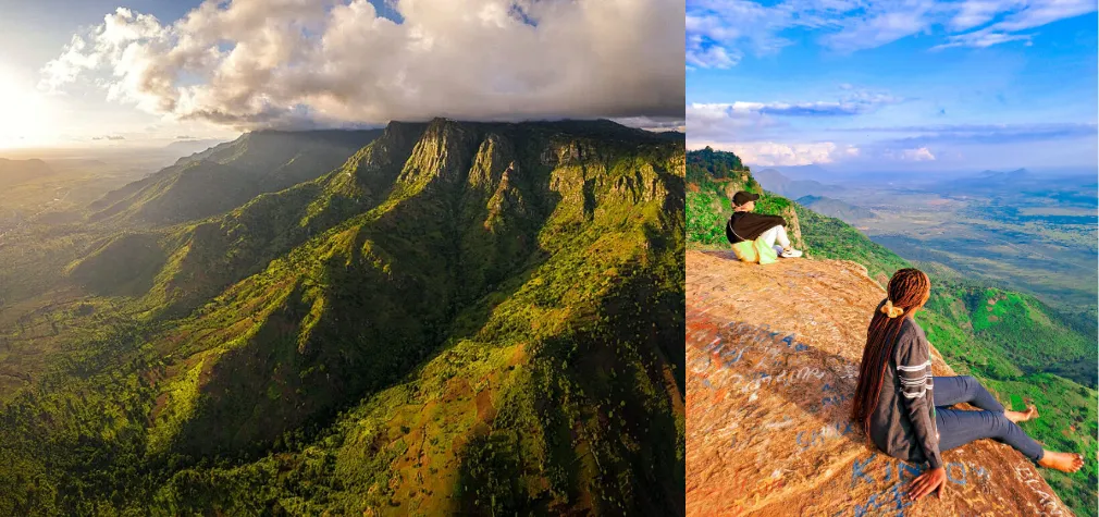 Two people sit on a rocky ledge at Irente Viewpoint, overlooking the lush Usambara mountains ridge and a vast mountainous landscape under a bright blue sky with scattered clouds.