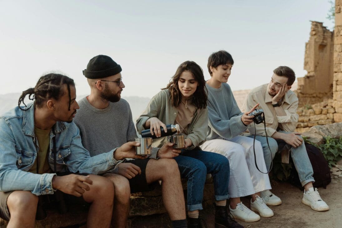 A small group of travelers sitting outdoors in a line during a welcome briefing, listening attentively to their guide.