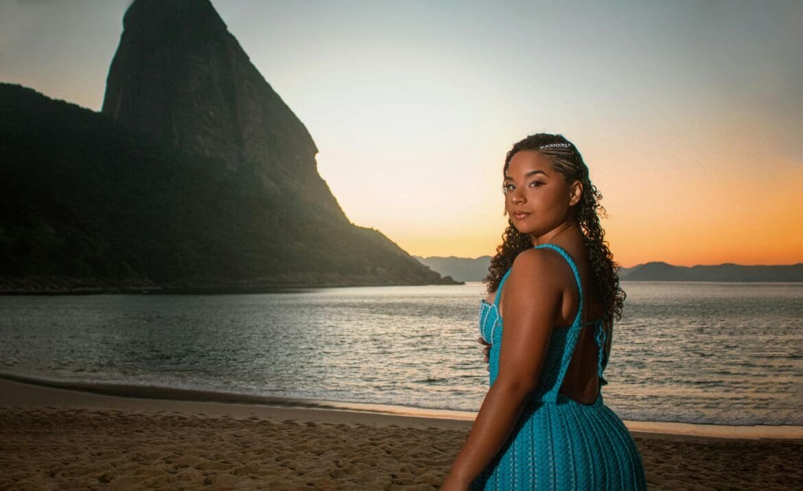 Woman with curly hair standing on the beach at sunset, showcasing a vacation-ready hairstyle that holds up in humid weather.