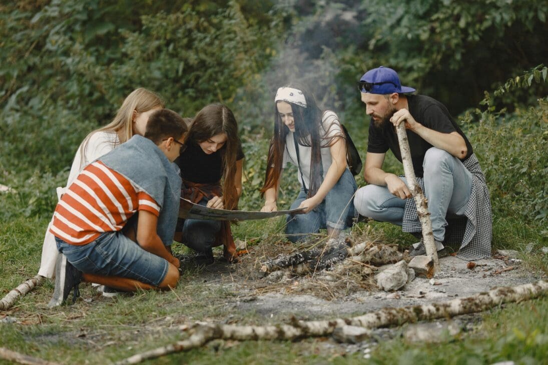 A small group of travelers working together to start a campfire in the woods.