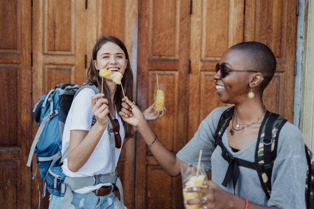 Two women laughing and enjoying street food together during their travels.