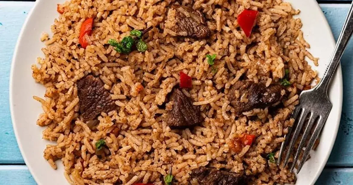 Close-up of a plate of Kenyan Pilau, a traditional spiced rice dish mixed with pieces of meat (likely beef) and vegetables, representing the culinary journey of Mombasa travel.