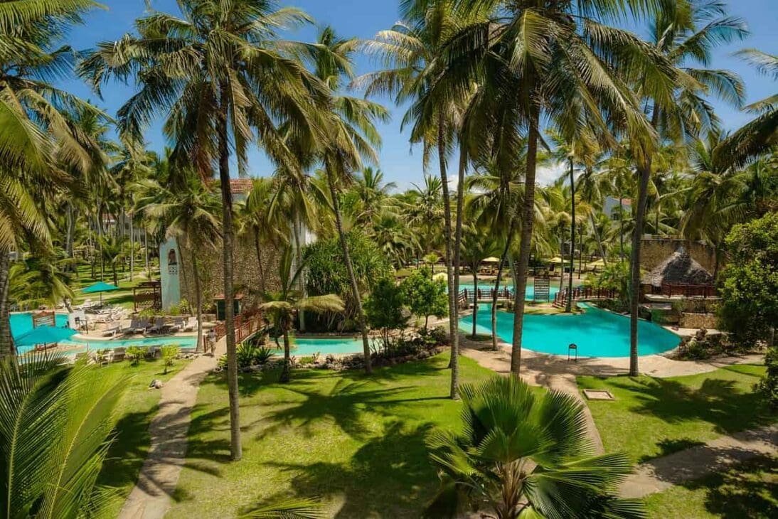 Resort swimming pools and surrounding vibrant green gardens and palm trees at Qwetu Beach Resort, offering a relaxing base for Mombasa travel.