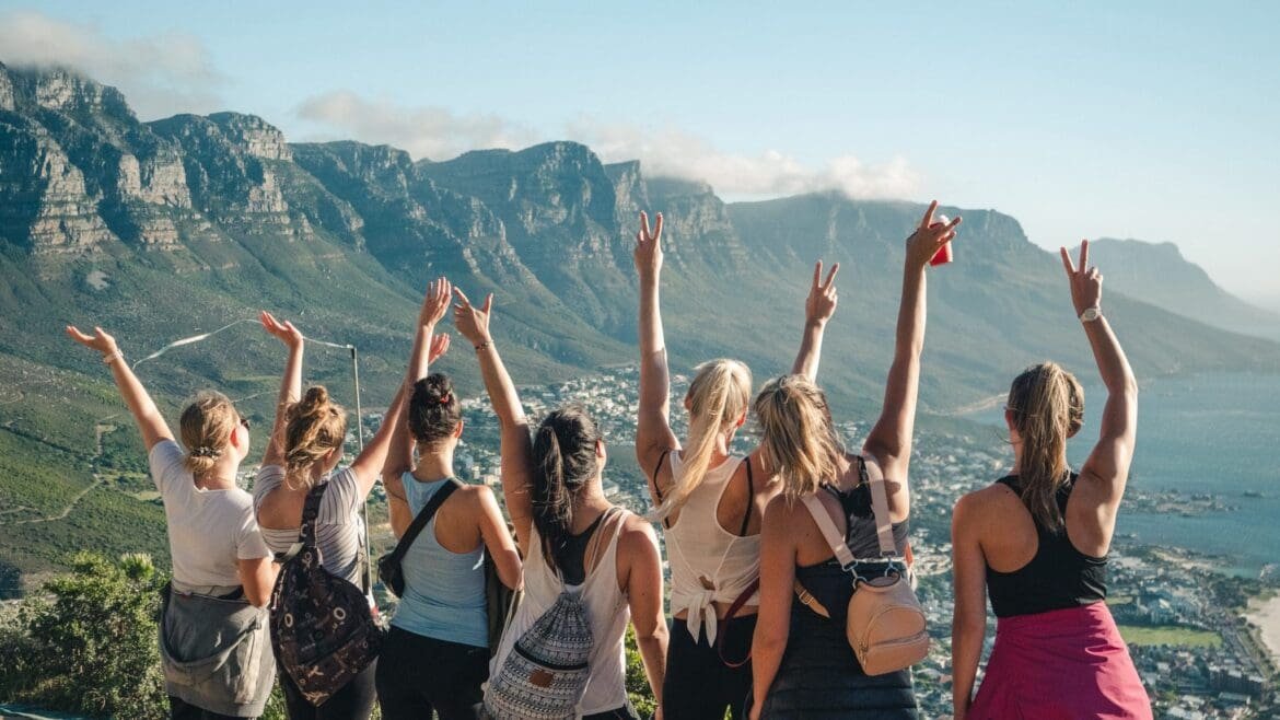 A small group of travelers standing on a scenic overlook, arms raised in celebration and enjoying the view together.
