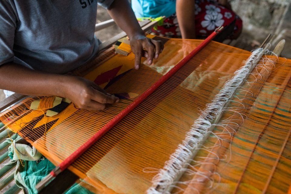 Balinese artisan weaving traditional fabric by hand in a Bali villages workshop, showcasing the island’s living craft heritage.