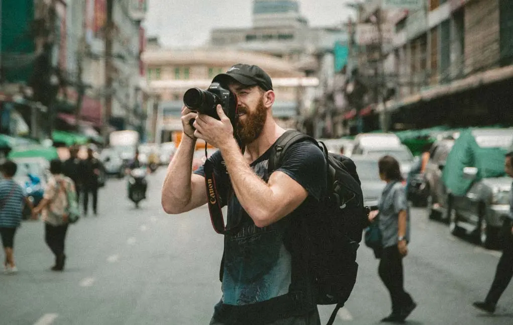 Photographer capturing a colorful cobblestone street at golden hour, with warm light highlighting buildings and subtle street activity.
