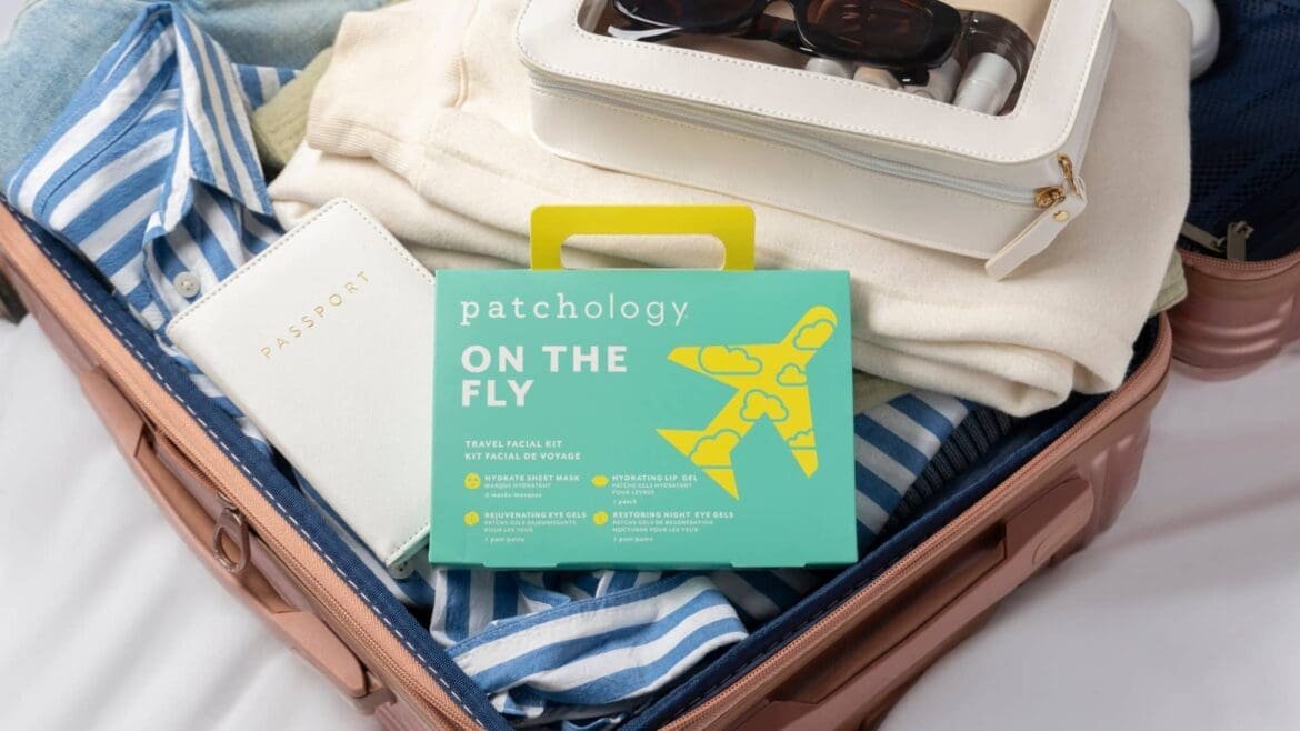 Minimalist flat lay of travel-sized skincare essentials on a hotel desk, including cleanser, moisturizer, SPF, and eye cream beside a passport, phone showing an off-time clock, and a sleep mask during jet-lagged travel.