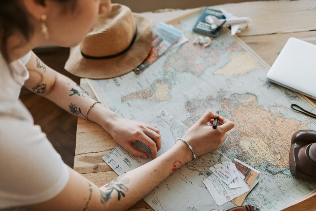 Flat-lay travel planning scene with a laptop showing film location maps, a camera, passport, coffee, and notes referencing movie and TV show destinations famous film location tours