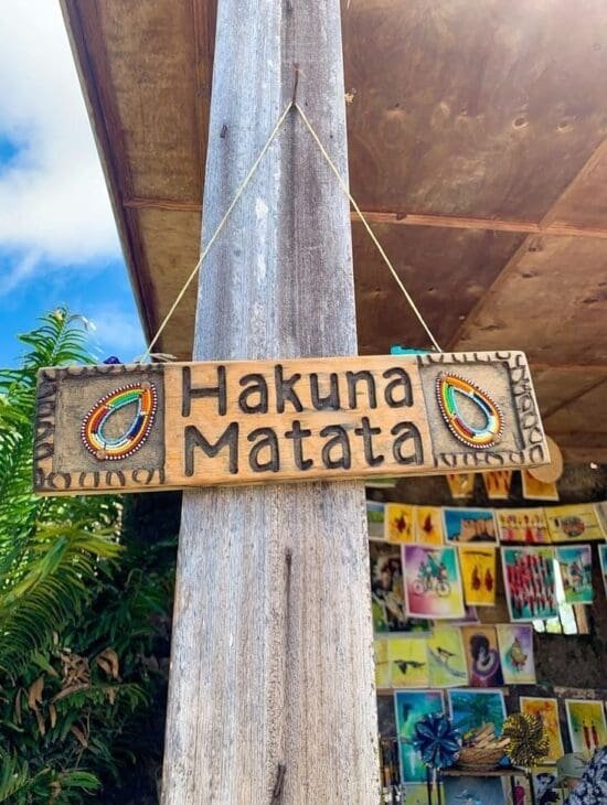 A wooden sign hanging on a post reads "Hakuna Matata" and is decorated with colorful Maasai beadwork circles.