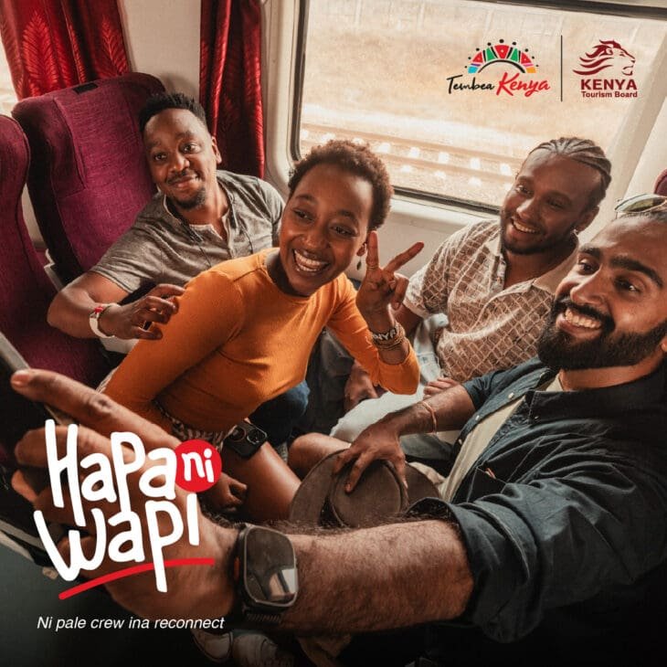 A group of four diverse friends smiling and laughing while taking a selfie inside a train car. One woman in an orange shirt makes a peace sign as they pose together near a window showing passing tracks. The image features the "Tembea Kenya" and "Kenya Tourism Board" logos, with stylized text in the foreground that reads "Hapa ni Wapi" and "Ni pale crew ina reconnect".