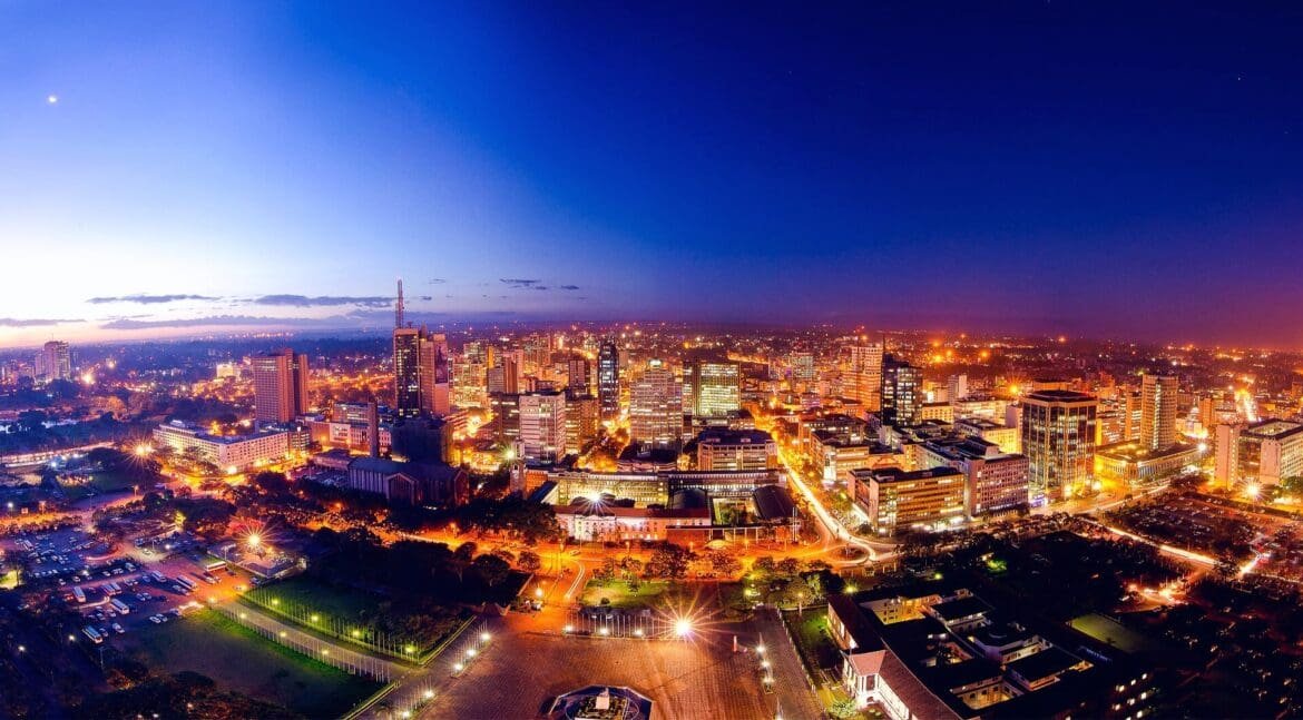 A wide-angle panoramic view of the Nairobi night skyline at dusk, with city lights twinkling under a deep blue and purple sky.