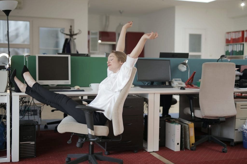 Person working at a home desk with visual cues for movement, including a yoga mat, water bottle, and exercise break reminders.