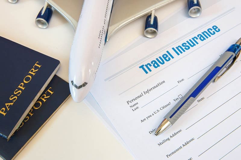 Top-down view of a travel insurance claim form, a blue passport, a pen, and a model airplane on a white surface.