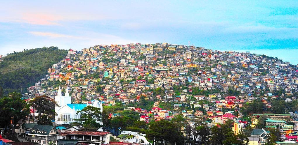 Panoramic peak view of Baguio City from the mountains, showcasing pine trees, rolling hills, and misty landscapes