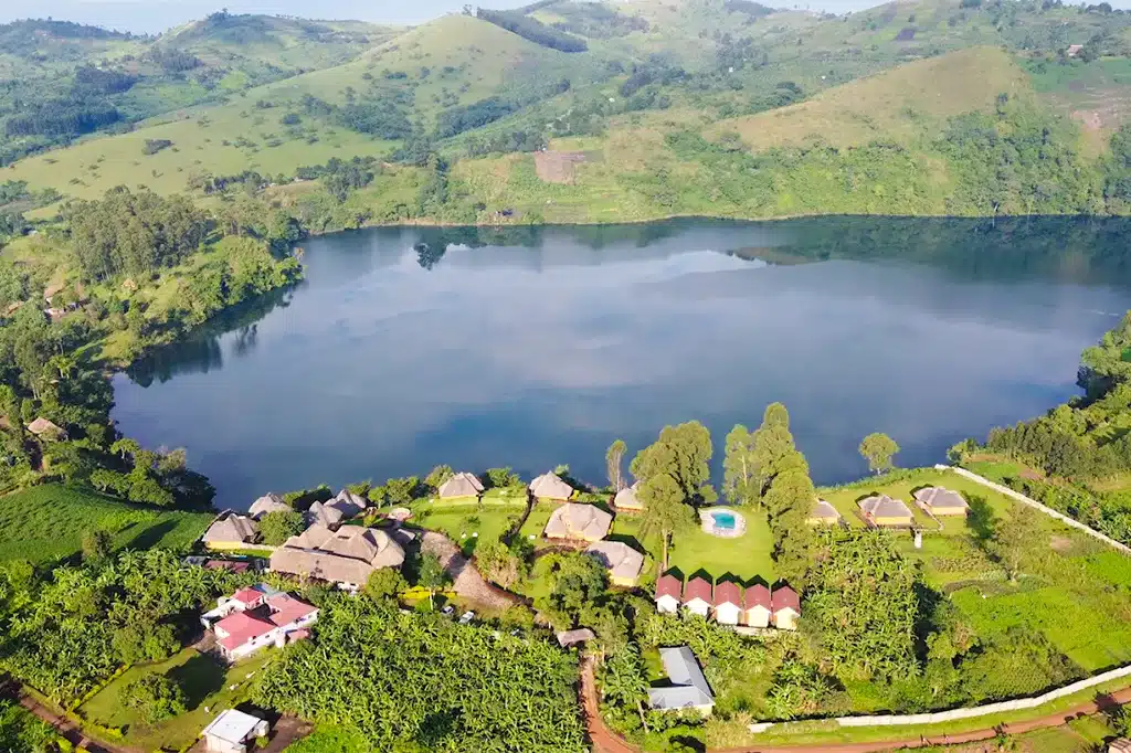 A cozy, thatched-roof eco-lodge nestled on a lush green ridge overlooking the serene blue waters of Victoria lake