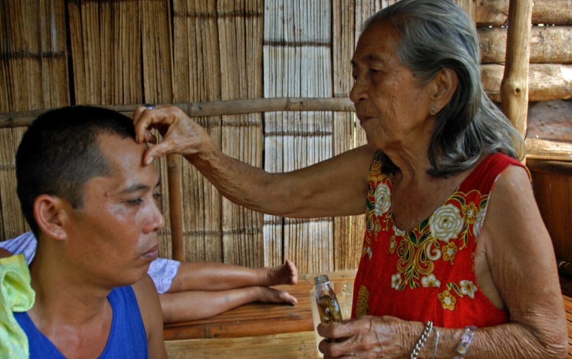 Traditional Filipino healer (manghihilot) practicing hilot using herbal oil in a rural Philippines setting.