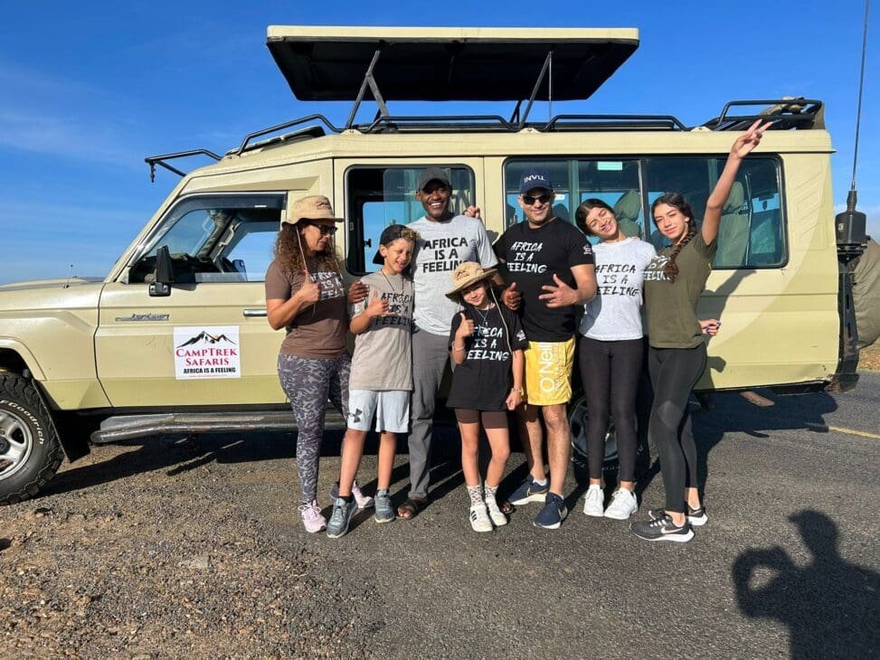 Tourists observing wildlife in East Africa with a 4×4 safari vehicle in the background.