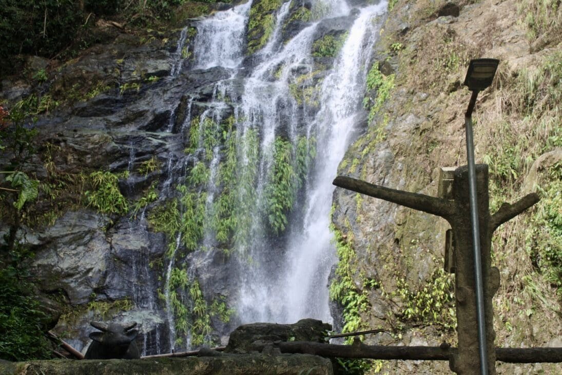 View of Tamaraw Falls in Puerto Galera, Oriental Mindoro, Philippines, with twin streams cascading into a lush tropical landscape.