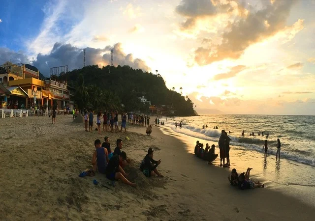Friends walking along White Beach in Puerto Galera at sunset, leaving footprints in the sand.