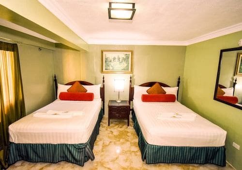 Two hotel beds side by side in Puerto Galera with soft morning light and open windows.