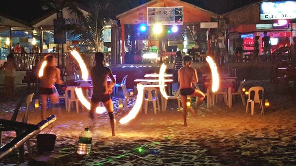 Night market in Puerto Galera with colorful food stalls, fire dancers, and visitors enjoying grilled seafood under string lights.