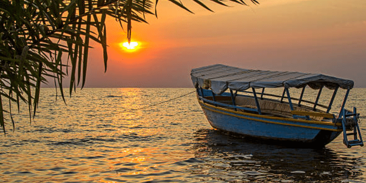Travelers enjoy the serene view of Lake Victoria during the dry season, with calm waters, fishing boats, and lush green shores under a clear sky.